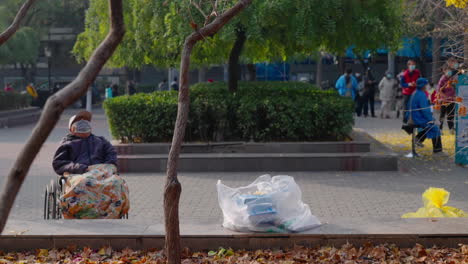 An-old-man,-wearing-a-mask,-rests-in-his-wheelchair-at-the-park-during-the-COVID-lockdown-in-Beijing,-China