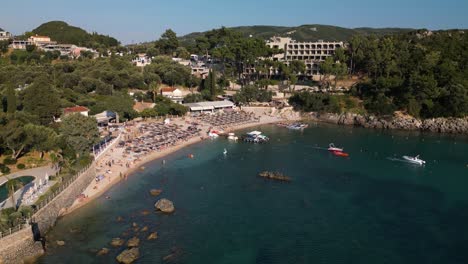 Eine-Drohne-Steigt-über-Das-Wasser,-Um-Zu-Zeigen,-Wie-Ein-Boot-Den-Hafen-Verlässt,-Während-Touristen-Auf-Korfu,-Griechenland,-Spielen-Und-Entspannen