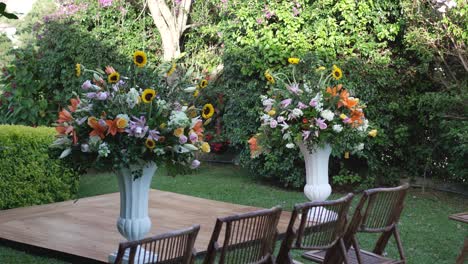 A-beautiful-garden-with-two-vases-of-flowers-with-bamboo-chairs-around-them,-set-for-a-wedding-celebration