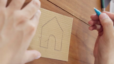 Close-up-of-hand-drawing-a-house-on-cardboard