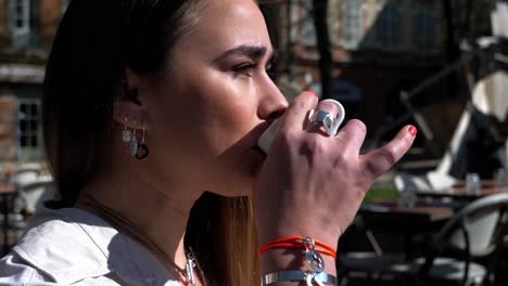 A-pretty-young-woman-on-the-terrace-takes-her-coffee-from-the-table-and-takes-it-to-her-mouth-to-drink