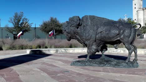 Estatua-De-Búfalo-Con-Banderas-Del-Estado-De-Texas-Moviéndose-Al-Fondo-En-Frontier-Texas-En-Abilene,-Texas-Con-Video-Estable