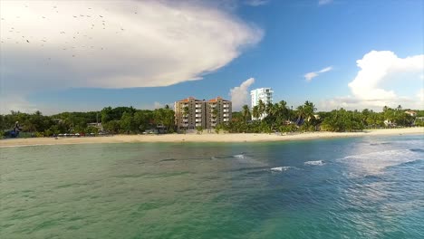 Approaching-drone-shot-of-the-picturesque-shoreline-of-Miami-Beach,-showing-some-luxurious-hotels,-beachgoers-swimming-and-some-birds-flying-in-the-sky,-in-Itea,-Greece