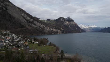 Schweizer-Häuser-Entlang-Des-Seeufers-Mit-Blick-Auf-Die-Straße,-Die-Den-Konturen-Der-Berge-Folgt