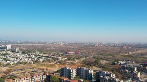Aerial-pan-shot-of-Islamabad,-with-residential-buildings,-highway-traffic,-and-metro-station-with-a-large-cityscape-of-twin-cities
