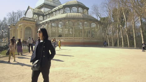 Woman-exploring-the-Palacio-de-Cristal-on-a-sunny-day-in-Retiro-Park,-Madrid,-surrounded-by-leisurely-visitors