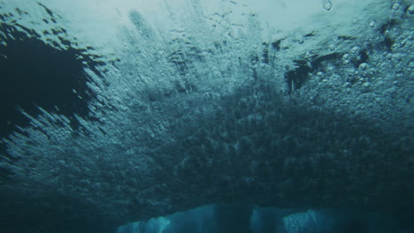 Türkisfarbene-Unterwasser-Winkelstruktur-Einer-Brechenden-Welle,-Die-Blasen-über-Die-Oberfläche-Und-Wasserwolken-Verteilt