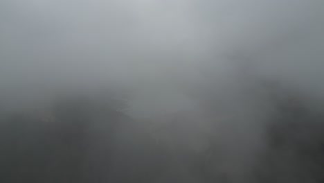 Aerial-pullback-between-misty-clouds-hides-reservoir-lake-in-alpine-mountain-region