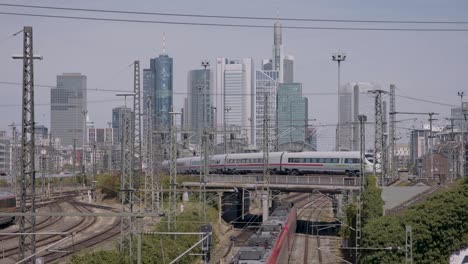 ICE-train-crossing-bridge-in-urban-area-with-city-skyline-in-daylight,-clear-skies