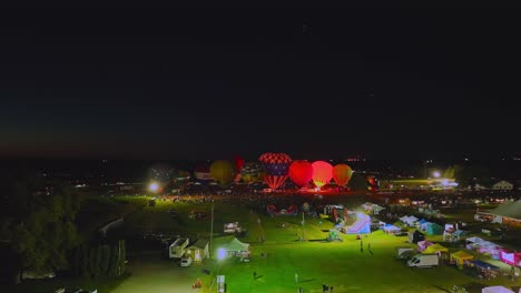 Aerial-View-of-a-Line-of-Performing-Hot-Air-Balloons-Glow-on-a-Summer-Evening
