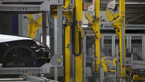 Black-car-on-assembly-line-with-robotic-arms-in-modern-automotive-factory,-industrial-setting