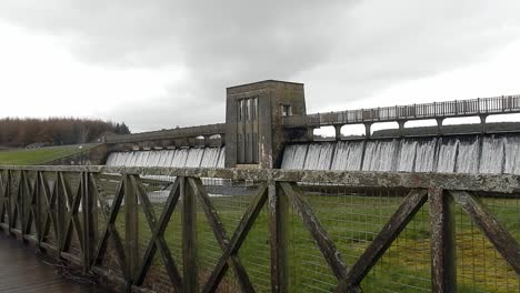 Llyn-Cefni-reservoir-dam-gate-overflowing-from-Llangefni-lagoon-surrounded-by-wooden-fencing