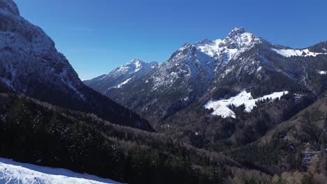 La-Mosca-De-Drones-Pasó-Por-Un-Camino-Nevado-Hacia-Un-Bosque-De-Pinos-Con-Enormes-Montañas-Con-Cumbres-Cubiertas-De-Nieve-En-El-Fondo-En-Austria