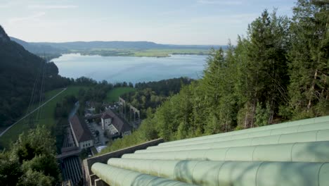 Elevated-view-of-large-green-pipes-with-forest-and-lake-in-the-background,-under-clear-skies