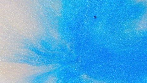 Vibrant-blue-ink-expanding-in-clear-water,-creating-an-abstract-diffusion-pattern,-high-angle-shot