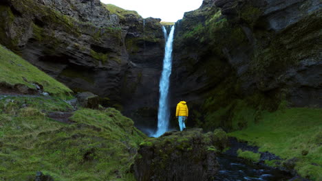 Mann-Steht-Auf-Dem-Felsen,-Um-Die-Schönheit-Des-Kvernufoss-Wasserfalls-In-Island-Zu-Bewundern
