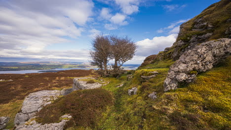 Panorama-motion-timelapse-of-rural-landscape-with-rocks,-trees-and-sheep-in-a-bog-field-and-hills-and-lake-in-distance-during-sunny-cloudy-day-viewed-from-Carrowkeel-in-county-Sligo-in-Ireland