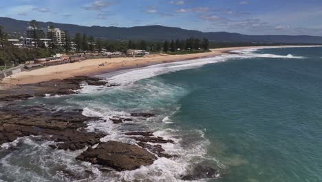 Over-rocks-and-surf-towards-the-surf-life-saving-facilities-at-North-Wollongong-Beach-with-buildings-in-the-background