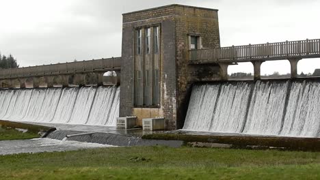 Llyn-Cefni-reservoir-concrete-dam-gate-overflowing-from-Llangefni-lagoon,-Anglesey-rural-scene