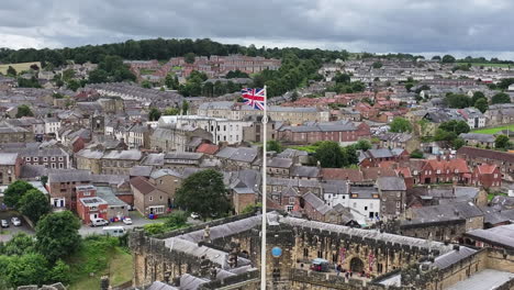 Luftaufnahme-Der-Britischen-Flagge,-Die-Auf-Einem-Mast-über-Der-Mittelalterlichen-Burg-Und-Stadt-Alnwick-Weht,-England,-Großbritannien