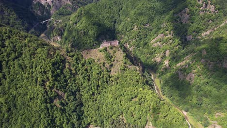 Poenari-Citadel-ruins-with-Vidraru-Dam-in-foreground,-surrounded-by-the-majestic-Fagaras-Mountains,-under-a-clear-sky
