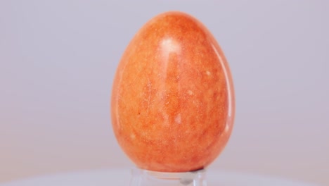 Orangefarbenes-Marmor-Ei,-Das-Sich-Langsam-Auf-Einem-Drehteller-Vor-Einem-Weißen-Hintergrund-Dreht