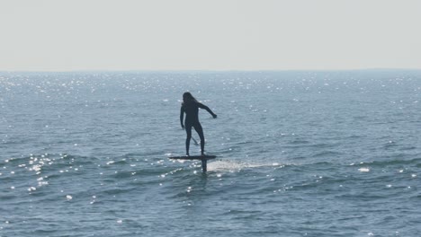 Sunny-Day-Adventure:-Man-Gliding-on-Jet-Surfboard,-Riding-Waves-with-the-Company-of-Birds-on-a-Serene-Coastal-Scene