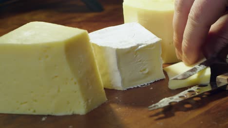 Three-cheese-blocks-on-cutting-board:-Wedge-of-Gouda-cheese-is-sliced