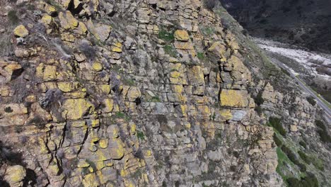 slow-moving-reveal-from-behind-yellow-fungus-covered-rocks-to-the-California-highway-38-valley-road-leading-to-forest-falls-with-dramatic-shadows-of-mountains-and-cars-passing-by-AERIAL-REVEAL-60FPS