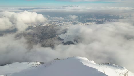 Vista-Aérea-Sobre-Las-Montañas-De-Piatra-Craiului,-Picos-Cubiertos-De-Nieve-Que-Atraviesan-Nubes-Blancas