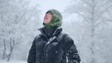 beautiful-woman-wearing-green-headgear-and-black-jacket-in-the-forest-with-melting-snow-falling-from-the-trees,-panning-slow-motion-footage