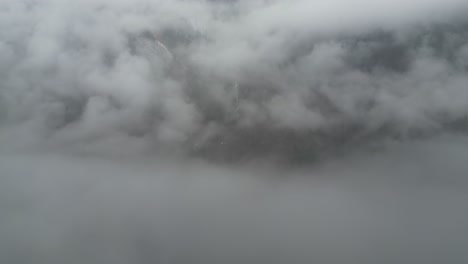 Misty-thick-grey-clouds-shroud-rugged-mountain-peak-with-snow-in-valley-ridges