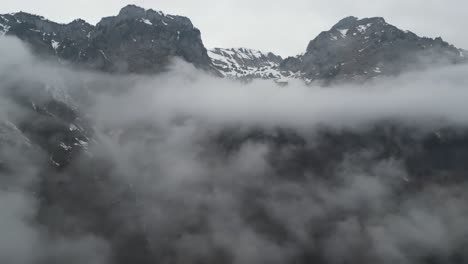 Nebelige-Wolken-Hängen-Tief,-Während-Epische-Bergrückenfelsen-Mit-Schnee-In-Den-Himmel-Ragen