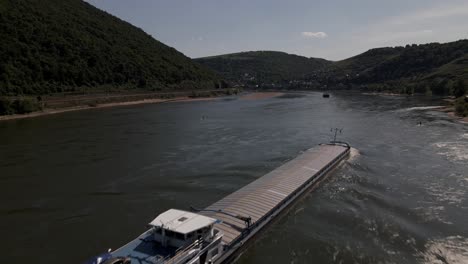 Barge-flatbottom-boat-being-pushed-by-a-tugboat-down-the-Rhine-River-in-Oberwesel,-Germany