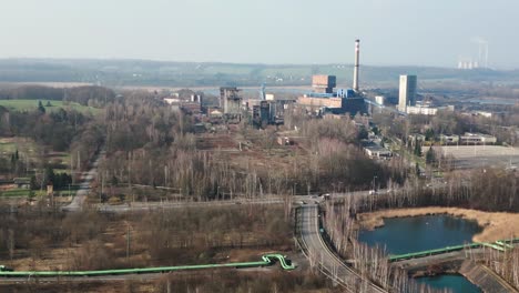 An-industrial-coal-mine-complex-surrounded-by-greenery,-with-tall-chimneys-belching-smoke,-large-buildings-and-a-road-running-through-the-countryside