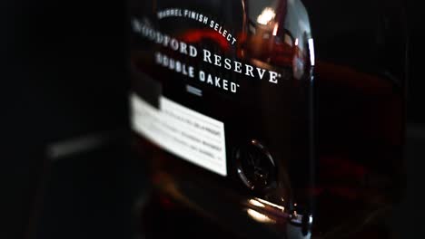 Schwenken-Auf-Einer-Flasche-Woodford-Reserve-Doppelt-Eichenholzgelagertem-Kentucky-Straight-Bourbon-Whiskey-Geringe-Schärfentiefe-Mit-Schwarzem-Hintergrund