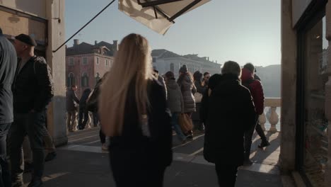 Bustling-Crowd-strolling-by-Venetian-shops-at-dusk,-on-top-of-Rialto-Bridge