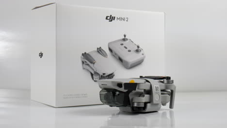 Neue-Gefaltete-DJI-Mini-2-Drohne-Neben-Paketbox,-Studioaufnahme-Mit-Weißem-Hintergrund