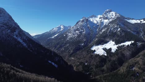 Vista-Aérea-Sobre-Un-Bosque-De-Pinos-Entre-Un-Enorme-Paisaje-Montañoso-A-Finales-Del-Invierno-En-Austria