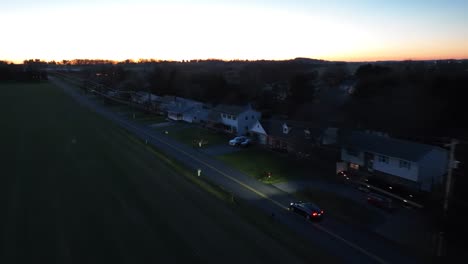 Toma-Aérea-De-Seguimiento-Del-Modelo-Tesla-Y-Conduciendo-Por-Una-Carretera-Residencial-Suburbana-Al-Atardecer