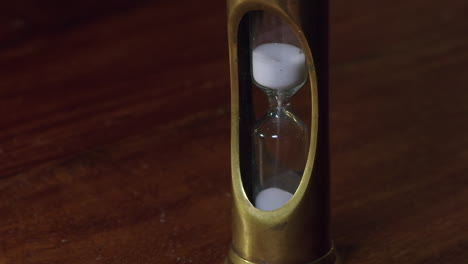 Time-passes,-granules-sift-through-brass-hour-glass-timer-on-wood-desk