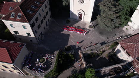 Drone-Shot-of-Majorette-Girls-Waving-With-Pom-Poms-in-Front-of-Church-in-Herceg-Novi,-Montenegro