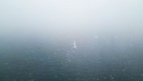 Drone-shot-of-sailing-boat,-driving-across-remote,-misty-sea,-during-a-snow-storm