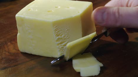 Right-hand-with-small-knife-cuts-slices-off-block-of-Swiss-cheese