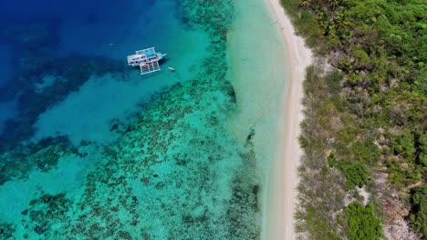 Drone-footage-of-a-white-beach,-turquoise-lagoon-and-a-boat-near-Palawan-in-the-Philippines