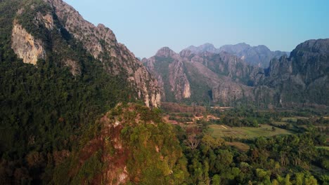 Limestone-formations-in-rural-countryside,-with-Laos-flag-on-hill