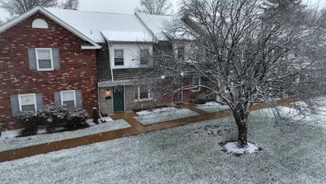 Red-brick-house-with-snowy-front-yard-and-adjacent-row-of-townhouses-during-snow-flurries