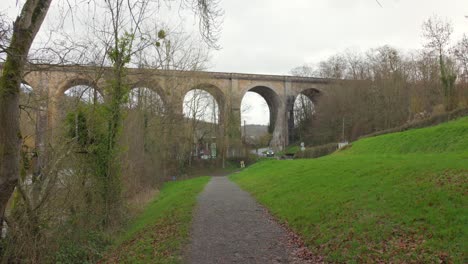 Ancient-viaduct-towering-over-lush-greenery-on-a-cloudy-day-in-Normandy,-France,-with-a-gravel-path