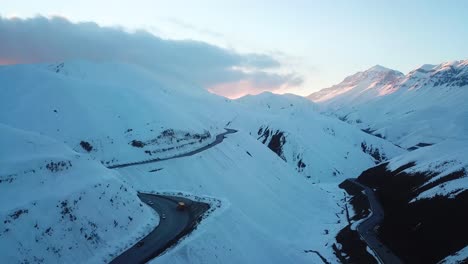 Luftaufnahme-Einer-Drohne,-Flug-über-Schneebedeckte-Berge-Mit-Blick-Auf-Die-Wunderbare-Rote-Sonnenuntergangslandschaft-Und-Die-Kurvenreiche-Straße-Auf-Dem-Land,-Winterreisen-In-Der-Kalten-Schneesaison-In-Der-Wilden-Natur,-Die-Malerische-Landschaft