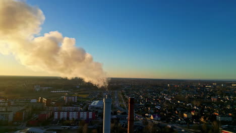 Aerial-parallax-closeup-with-industrial-factory-tower-in-the-foreground,-vivid-sunset-through-smoke